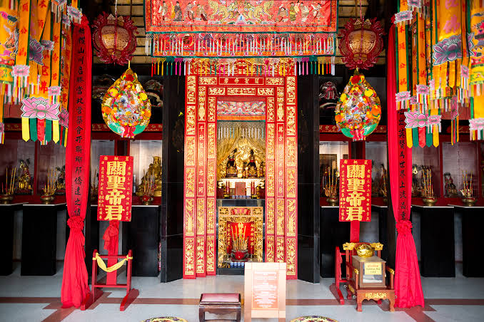 Koh Samui déli részén, Hua Thanon településén található a sziget egyik legkülönlegesebb kulturális látnivalója, a Guan Yu Shrine. Már az útról messziről feltűnik a hatalmas, vörös arcú Guan Yu-szobor, amely 16 méteres magasságával uralja a szentély előtti teret.

A hely egészen más hangulatot áraszt, mint Koh Samui thai buddhista templomai. A vörös és arany színek, kínai motívumok, sárkányábrázolások és a monumentális harcos szobra a sziget jelentős kínai–hainani kulturális örökségét mutatja be.

Ki volt Guan Yu?

Guan Yu a kínai történelem egyik legendás hadvezére volt, aki a Három Királyság korában élt. Az évszázadok során történelmi személyből tisztelt istenséggé vált, és különösen a hűség, becsület, igazságosság és bátorság jelképeként tisztelik.

Ábrázolásain könnyű felismerni: vörös arc, hosszú fekete szakáll és tradicionális kínai harcos öltözet jellemzi. Guan Yu szentélyei ma Kínán kívül is számos olyan helyen megtalálhatók, ahol jelentős kínai közösségek alakultak ki.

A kínai közösség története Koh Samuin

A Guan Yu Shrine azért különösen érdekes, mert Koh Samui történetének egy olyan oldalát mutatja meg, amellyel sok turista egyáltalán nem találkozik.

A 19. századtól jelentős számú, főként Hainan szigetéről érkező kínai bevándorló telepedett le Koh Samuin. Kereskedelemmel és többek között kókusztermesztéssel foglalkoztak, miközben saját vallási és kulturális hagyományaikat is magukkal hozták.

A Hua Thanon környéki Guan Yu-szentély története több mint száz évre nyúlik vissza, és generációkon keresztül a helyi hainani közösség egyik fontos vallási és közösségi központja maradt.

A hatalmas Guan Yu-szobor

A hely legfeltűnőbb látványossága természetesen a 16 méter magas Guan Yu-szobor.

A monumentális alak vörös arca és hagyományos harcos megjelenése már a Ring Roadról is könnyen észrevehető. Közelről pedig még látványosabb a szobor mérete és részletgazdagsága.

Érdemes azonban nem csak a szobornál megállni. A szentély belső tereiben aranyszínű díszítések, kínai kalligráfia, sárkánymotívumok és vallási tárgyak láthatók, valamint a helyi kínai közösség történetéhez kapcsolódó régi fényképek is megtalálhatók.

Mire figyelj látogatáskor?

A Guan Yu Shrine ma is működő vallási hely, ezért ugyanúgy tisztelettel érdemes viselkedni, mint Koh Samui buddhista templomaiban.

A szentély nem hatalmas terület, ezért könnyen beilleszthető egy Lamai és a sziget déli része köré szervezett kirándulásba. A közeli Hin Ta & Hin Yai sziklákkal is jól kombinálható.

Mennyi időt érdemes rászánni?

Körülbelül 30–45 perc elegendő ahhoz, hogy nyugodtan körbejárd a szentélyt, megnézd a Guan Yu-szobrot és a részleteket, valamint készíts néhány fotót.

Ha érdekel Koh Samui történelme és a helyi kínai közösség kultúrája, érdemes ennél valamivel több időt hagyni rá.

Miért érdemes megnézni?

✓ Monumentális, 16 méter magas Guan Yu-szobor
✓ Koh Samui kínai–hainani kulturális örökségének fontos helyszíne
✓ Látványos vörös és arany kínai építészeti részletek
✓ Teljesen más hangulat, mint a sziget buddhista templomaiban
✓ Érdekes betekintés Koh Samui kevésbé ismert történelmébe
✓ Könnyen összeköthető Lamai és Hua Thanon más látnivalóival

Hasznos információk

Helyszín: Hua Thanon / Maret, Koh Samui
Típus: kínai szentély és kulturális látnivaló
Nyitvatartás: a jelenlegi helyadatok szerint naponta 09:00–17:00.
Időtartam: kb. 30–45 perc
Öltözet: vallási helyhez illő öltözet ajánlott
Megközelítés: közvetlenül Koh Samui Ring Roadja mellett, Hua Thanonban.